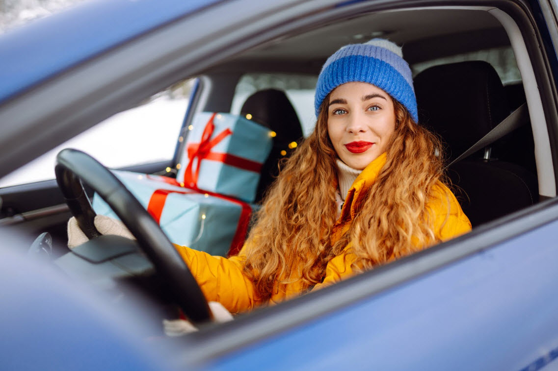 A woman behind the wheel of a car with presents in the passenger seat