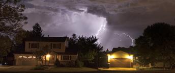 Houses lit by an approaching lighting storm.