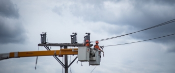 Two hydro workers performing repairs on a pole on a cloudy day