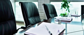 Three chairs around a meeting room table with notebooks and pens at the place settings.