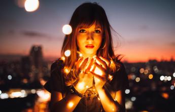 Woman holding lights against the backdrop of a city alight at night