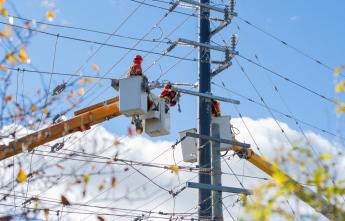 Powerline workers suspended in a bucket truck attend to a hydro pole