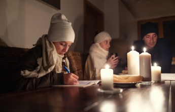 Young children and a man in winter clothing sit around a table with candles