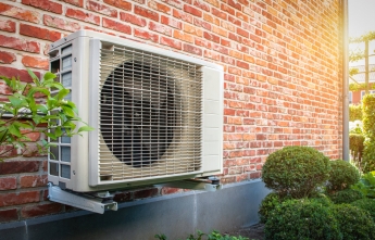 A heat pump on the side of a brick house on a sunny day