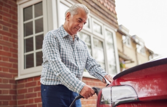 An older gentleman plugs in his electric vehicle outside his house