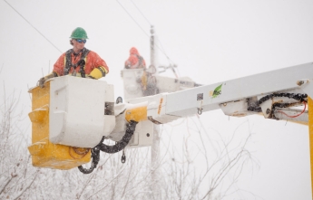Hydro Ottawa crews carried in boom trucks close to wires, work in a winter snowstorm