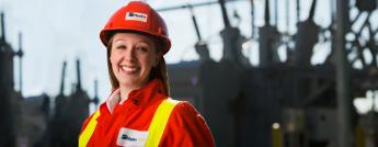 A female engineer dressed in personal protective clothing with a transformer station in the background