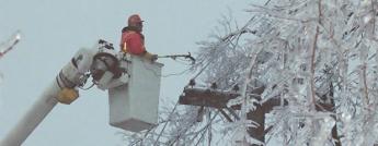 Photo of powerline maintainer in an aerial bucket surrounded by ice covered trees working to restore power in the aftermath of the 1998 Ice Storm.