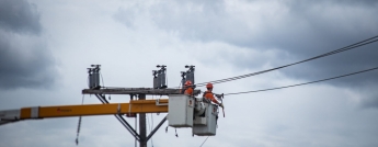 Two hydro workers performing repairs on a pole on a cloudy day