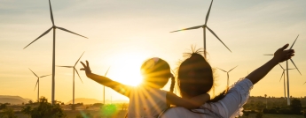 A mother and daughter at sunset with wind turbines in the distance