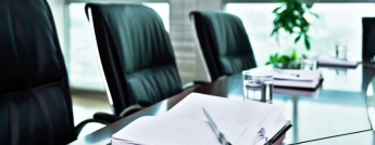 Three chairs around a meeting room table with notebooks and pens at the place settings.