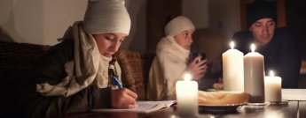 Young children and a man in winter clothing sit around a table with candles