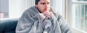 A man wears a warm hat and blanket inside his house
