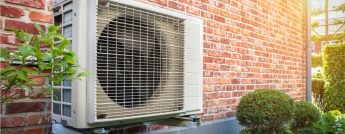 A heat pump on the side of a brick house on a sunny day