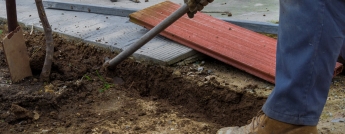 Worker digging a ditch with a hoe on a construction. Man in boots and safety gloves.