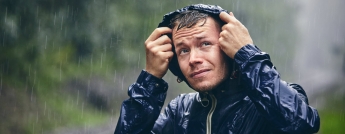 Young man in blue rain jacket getting drenched in heavy rain.