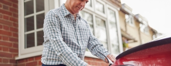 An older gentleman plugs in his electric vehicle outside his house