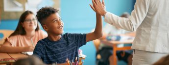 A young boy high-fives his teacher in class