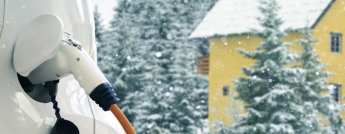 A yellow country house surrounded by trees in winter with a white electric vehicle charging in the foreground