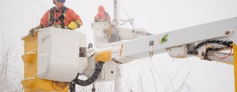 Hydro Ottawa crews carried in boom trucks close to wires, work in a winter snowstorm